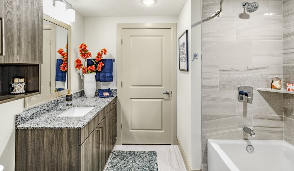 Large well lit bathroom with large mirror and white cabinets with a spacious walk in closet.